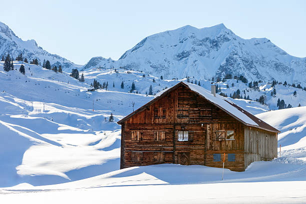 Mountain winter landscape with snow covered wooden shed in Austrian Alps.