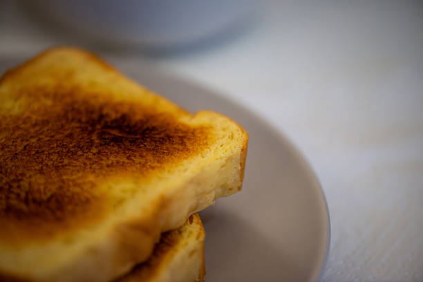 a freshly grilled ham and cheese sandwich on a white ceramic plate, placed on a white table next to a glass of natural orange juice