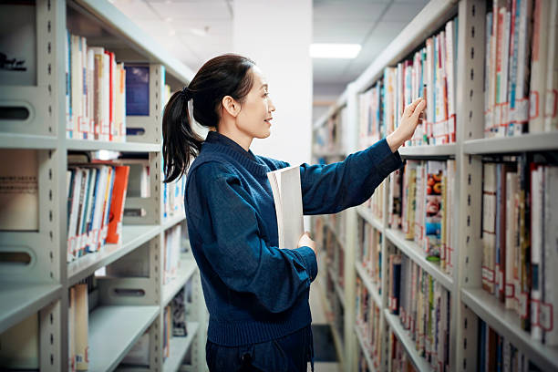 Woman Selecting Book in Library Shelves