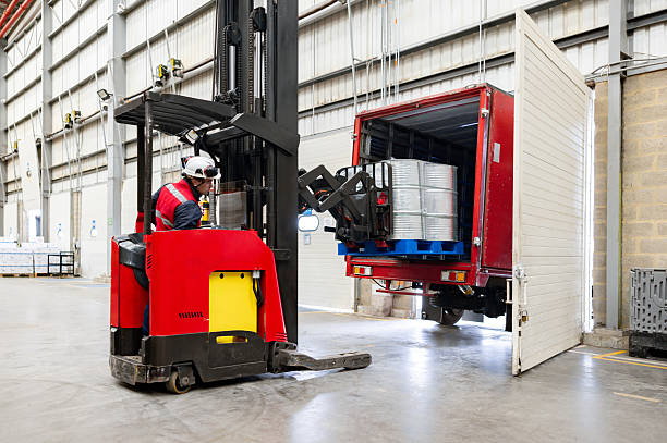 Latin American employee driving a forklift and loading barrels on a truck at a warehouse