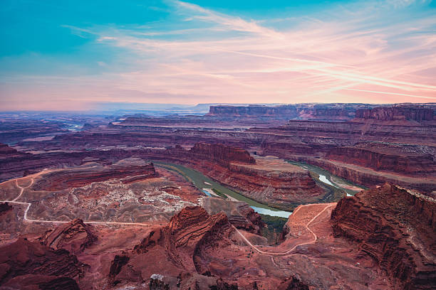 A breathtaking sunrise illuminates the dramatic curves of the Colorado River at Dead Horse Point State Park in Utah. The fiery orange and red hues of the canyon contrast with the deep shadows of the rugged terrain, capturing the raw beauty of the American Southwest in one of its most iconic viewpoints.