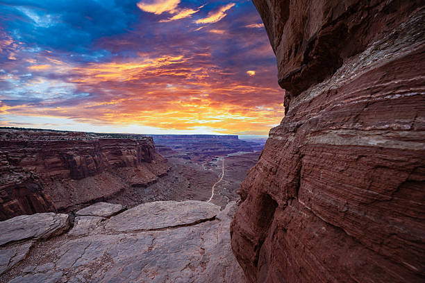 Vibrant sunrise light spills over the vast desert landscape of Canyonlands National Park in Utah, illuminating the rugged cliffs and winding Shafer Trail road below. This remote backcountry road offers a breathtaking view of red rock formations, deep canyons, and wide open skies — a signature scene of the American Southwest.