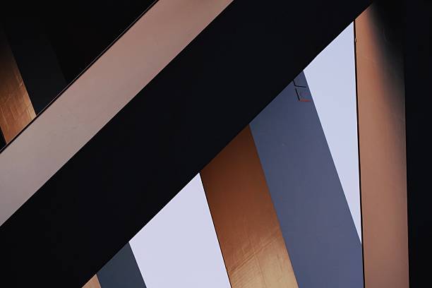 Striking low-angle architectural photograph featuring bold intersecting lines and planes of a contemporary building interior, with deep black shadows contrasting warm gold, cool gray, and soft beige panels creating a dynamic geometric composition full of depth and visual rhythm. This minimalist yet powerful image evokes modern design sophistication, urban elegance, and structural innovation, perfect for architecture publications, corporate branding, real estate marketing, design inspiration, abstract art prints, or stock use in technology, finance, and luxury lifestyle contexts. High-resolution capture with strong graphic contrast, rich tonal range, and precise geometry for maximum visual impact and broad commercial appeal.