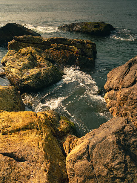 Close view of sea waves splashing over dark coastal rocks, creating dramatic water patterns and foam textures. Natural seascape showing the power and movement of ocean water along the rocky shoreline in Gokarna, Karnataka, India.
