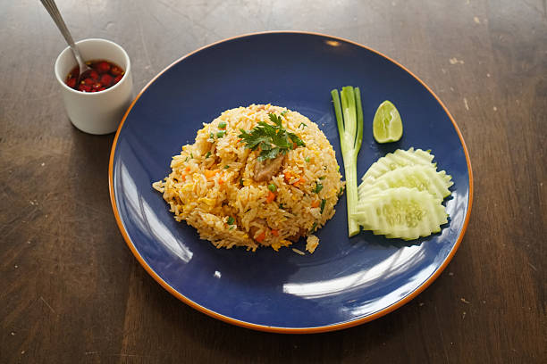 Thai fried rice with pork and mixed veggies, placed on a dark ceramic plate. Asian food fried rice with pork and egg