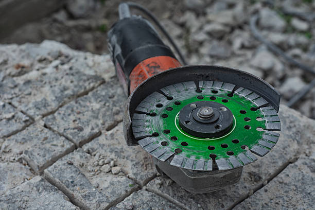 istock Close-up of an angle grinder with a green segmented diamond cutting disc placed on rough concrete paving stones. 2258436456