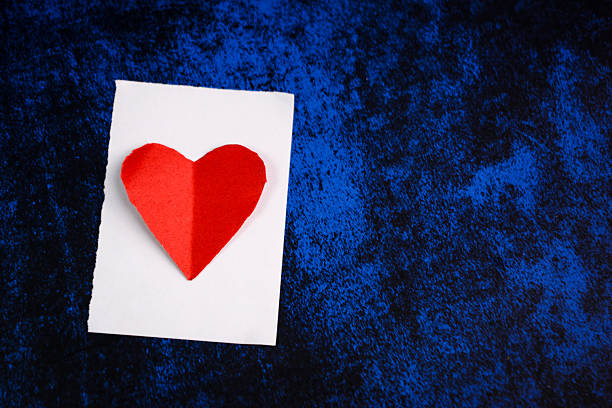 Minimal red heart placed on a dark background with subtle light, representing love, emotional wellbeing, healthcare, and heart health concepts.