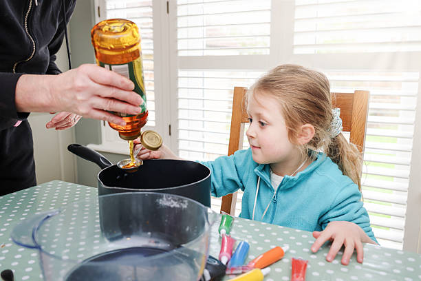 Five year old girl watching her Grandmother squeeze syrup into a bowl as they prepare to make Gingerbread shapes at a domestic kitchen table