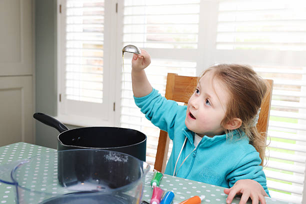 Five year old girl watches syrup pour from a spoon as she helps her Grandmother make gingerbread shapes at a domestic kitchen table