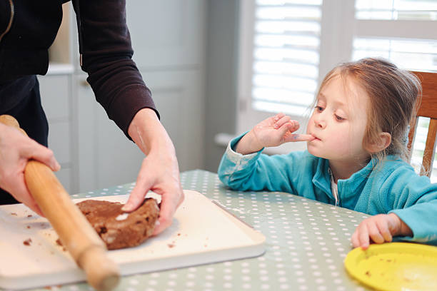 Five year old girl looking at her Grandmother roll out gingerbread dough as they prepare to make Gingerbread shapes at a domestic kitchen table