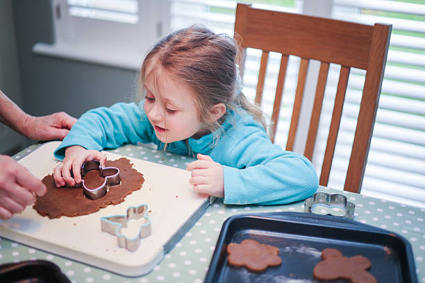 Five year old girl preparing and making Gingerbread shapes with her Grandmother at a domestic kitchen table