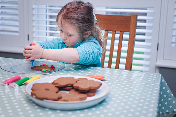 Five year old girl decorating her freshly baked gingerbread shapes with coloured icing with her Grandmother at a domestic kitchen table