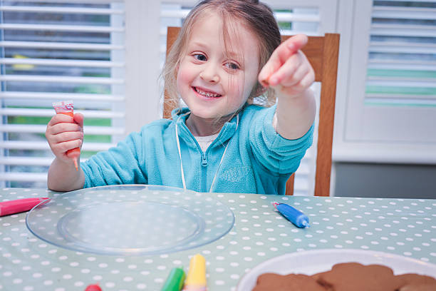 Five year old girl decorating her freshly baked gingerbread shapes with coloured icing with her Grandmother at a domestic kitchen table