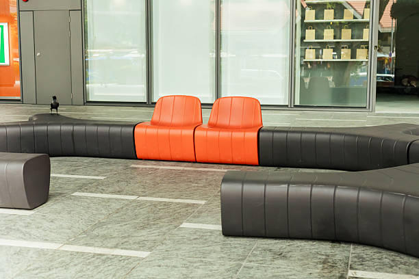 Two orange chairs are positioned in a curved gray seating area. The setting is indoors with abundant natural light. The space has a contemporary design.