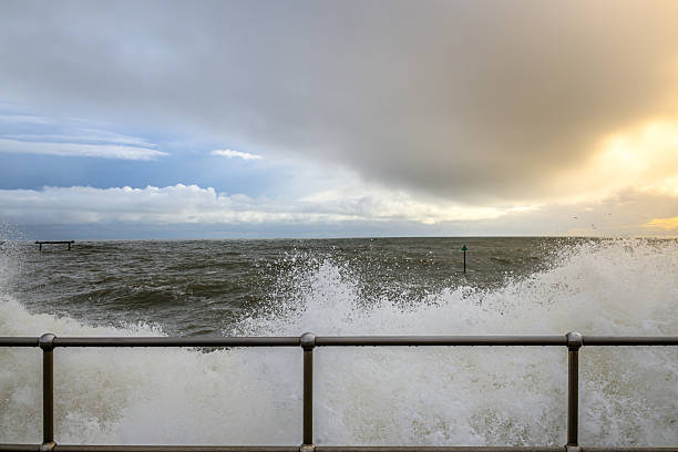 Crashing waves and dramatic sky with promenade railings