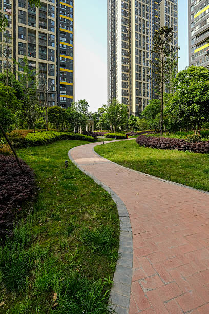 Vertical shot of a winding brick path cutting through green grass, leading the eye towards tall residential apartment buildings in the background.