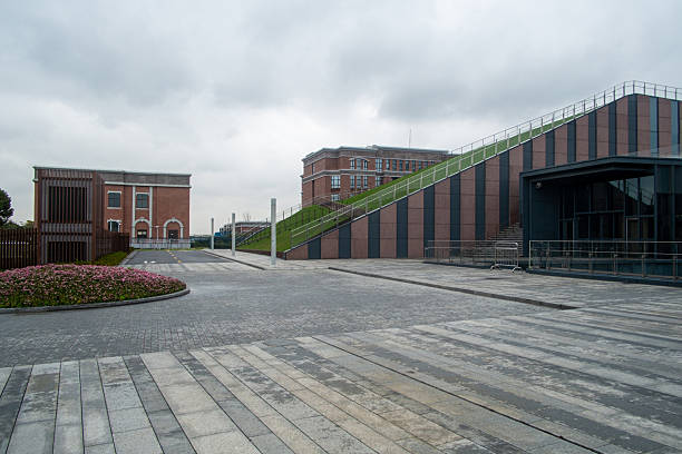 Wide angle view of a spacious paved public plaza featuring a red brick building and a unique grassy ramp structure leading to a roof level.