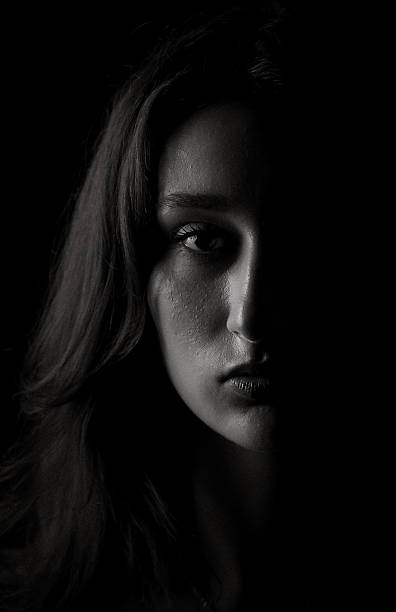 istock Young woman showing half face emerging from darkness 2258452547
