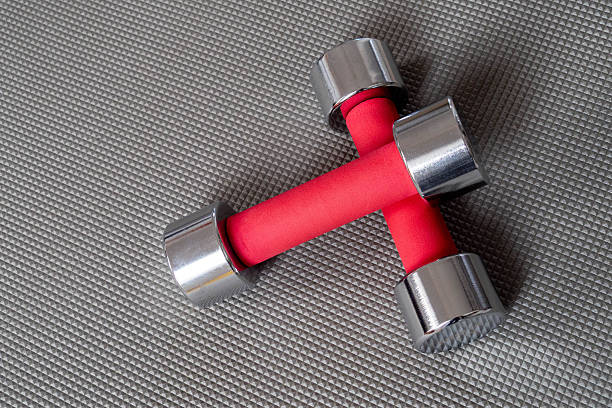 Two dumbbells with red handles are on a grey surface. The dumbbells are made of metal and have a shiny appearance