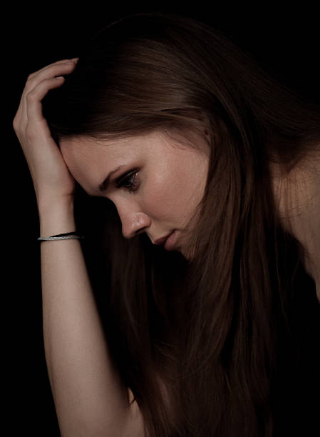Sad young woman suffering from a headache or depression is holding her head with hand on black background