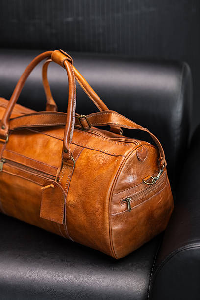 Premium tan leather duffel bag on a black leather sofa in a modern minimalist interior.