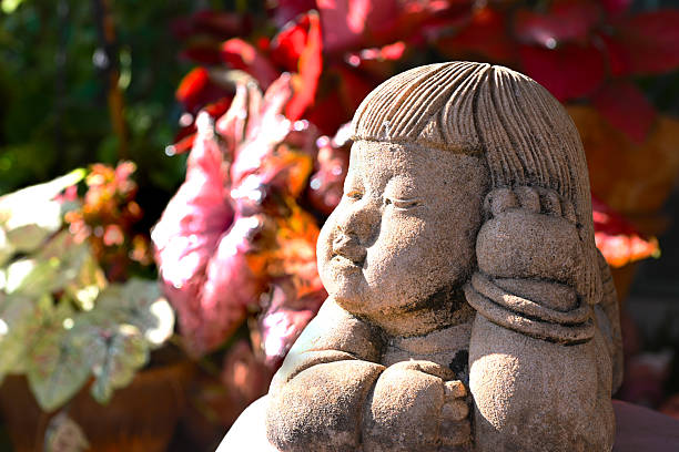 Photo of a small old plastic doll. It stands alone on a large stone surface. She is holding her hand to her cheek.  She is desperate.
