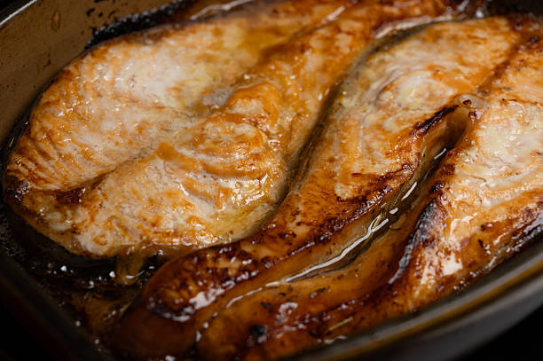 Close-up view of baked salmon steaks served in a ceramic baking dish. Freshly cooked seafood with golden texture, suitable for healthy food, home cooking, and gourmet cuisine concepts.