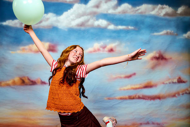 Happy girl with red hair holding a green balloon against a painted sky background