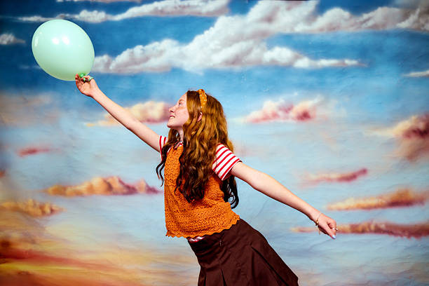 Red-haired girl reaching for the sky while holding a green balloon, expressing joy and freedom
