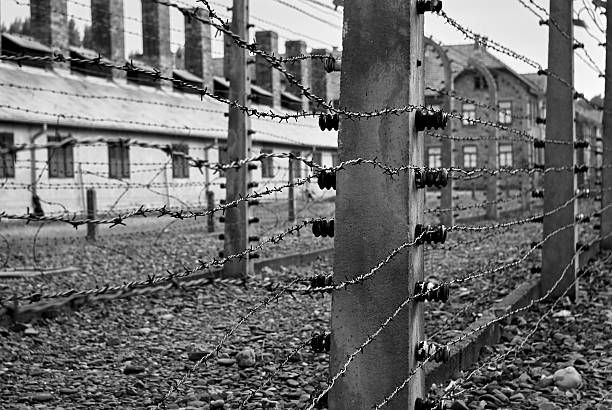 Close-up of barbed wire fence with brick barracks in background