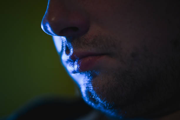 Man's profile highlighting chin and lips with blue light reflection in darkness