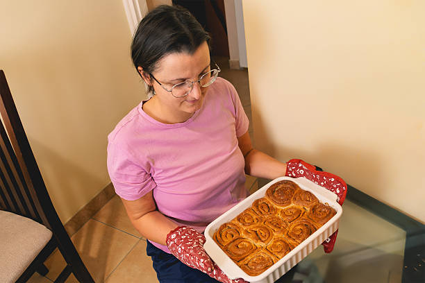 Caucasian female holding baked cinnamon rolls in kitchen setting