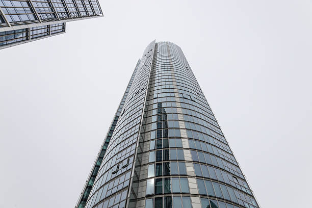 Worm's eye view of a curved glass skyscraper stretching towards an overcast sky in a business district. London, UK, 6 April 2024