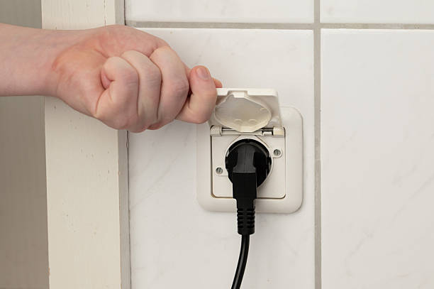 Hand lifting the hinged cover of a splash-proof IP44 Schuko wall socket on tiled bathroom wall, showing moisture protection and electrical safety in wet rooms.