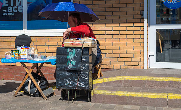Kyiv, Ukraine - 12th May, 2022: Street vendor standing next to a makeshift stall, selling various products like snacks and drinks under an umbrella for shade