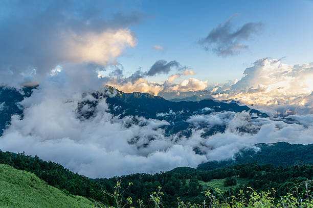 Thick clouds drift across forested slopes of Mountain Hehuan in Nantou Taiwan. A vivid early autumn scene under clear blue sky.