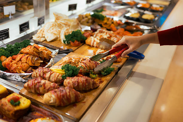 Person using tongs to serve from a diverse buffet spread in a catering setting, close-up of hand selecting hot dishes