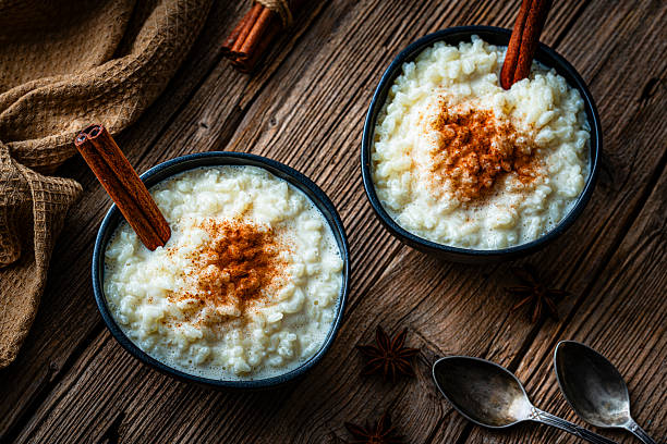 High angle view of two bowls of homemade rice porridge or pudding with cinnamon sticks on rustic wooden table. Sweet food or dessert