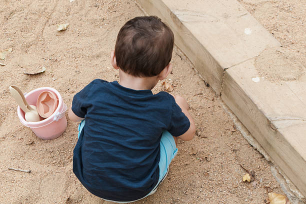 Child engrossed in creative play in a sandbox, using a toy bucket and shovel, fostering childhood development