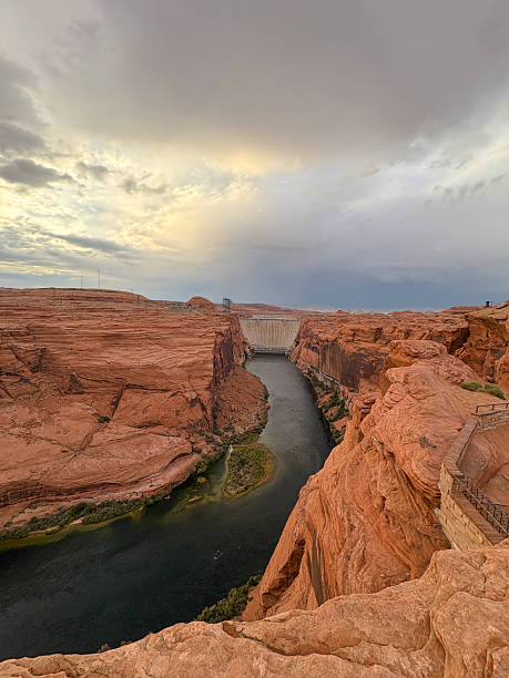 Scenic canyon landscape with a winding river and distant dam, showcasing dramatic rock formations, natural beauty, and expansive desert scenery at sunset.