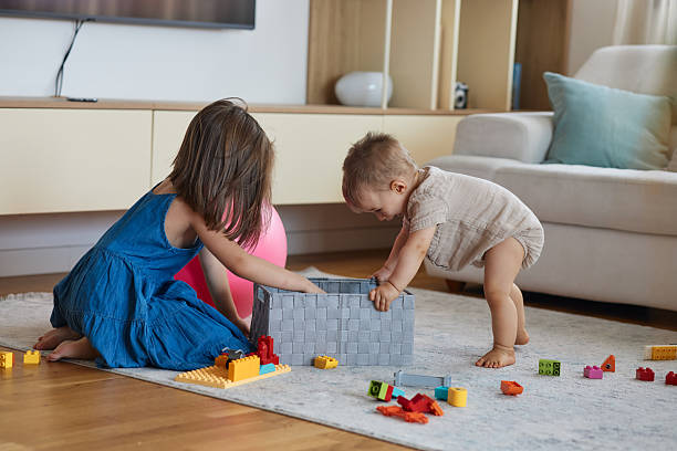 Two siblings playing with building blocks on a rug in a modern living room