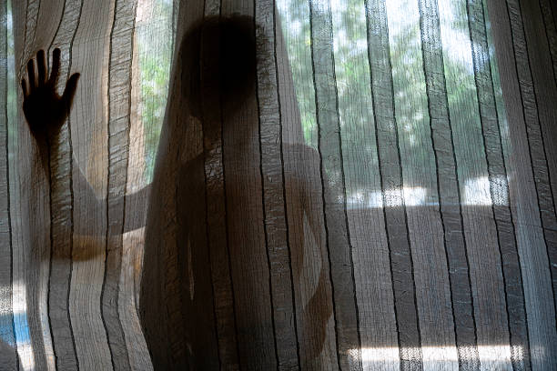 Child's silhouette hiding behind curtains with sunlight creating strong shadows