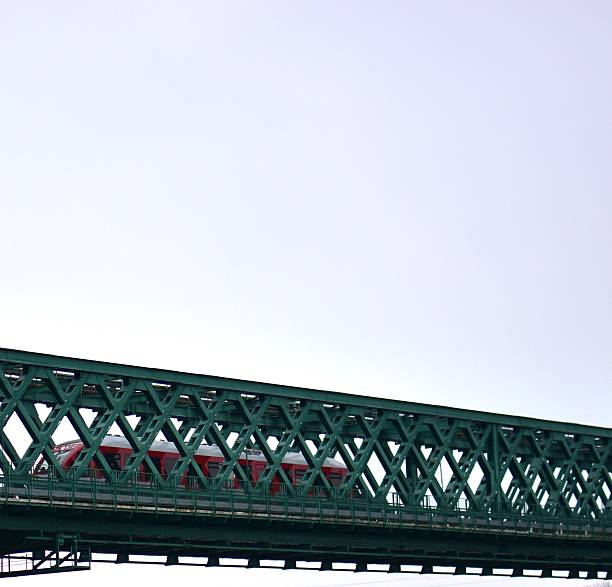 Passenger train crossing a steel truss bridge. Transportation and infrastructure concept, railway engineering, industrial structure against minimal sky background.