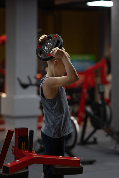 A teenager trains in a gym with a strength medicine ball. A young man holds a medicine ball in his hands