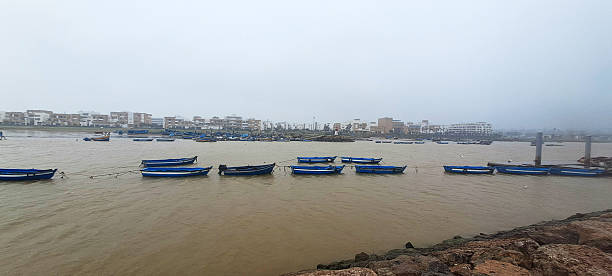 Rowboats floating on murky river water in a moroccan coastal town covered in fog