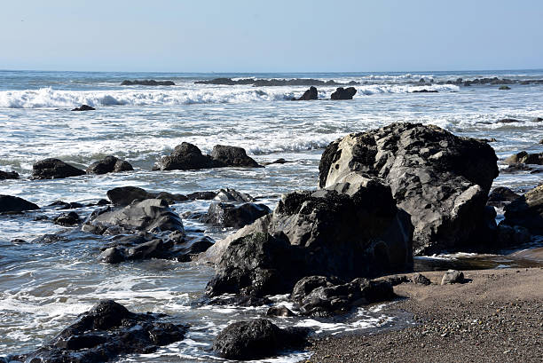 Tar pit rocks with waves rolling over asphalt in the ocean.