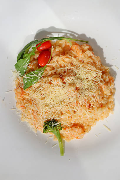 The image features a delicious shrimp risotto topped with grated cheese, two cherry tomatoes, arugula leaves, and a small broccoli floret on a white plate
