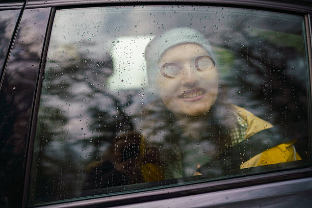 Woman in a car smiling looking out a rainy window with raindrops covering the glass.