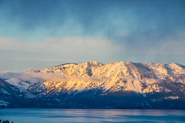Snow-capped mountains glow at sunset across the blue waters of Lake Tahoe in winter