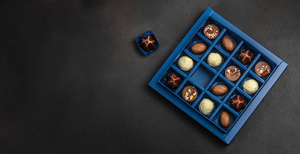 Luxury assorted chocolate pralines in elegant blue gift box with single chocolate candy on dark background and large copy space for advertising and branding